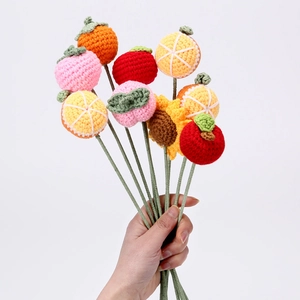 Detailed view of hand-knitted fruit charms showing orange, peach, and apple stitches