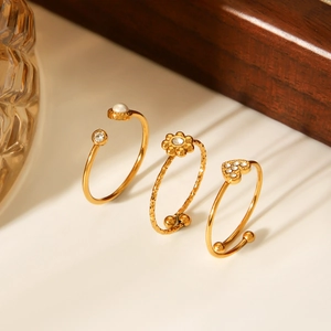 Détails de trois bagues dorées ajustables ornées de perles, fleurs et motifs de cœur