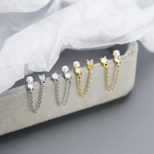 Detail of silver and gold chain earrings with pearls and cubic zirconia on a velvet stand