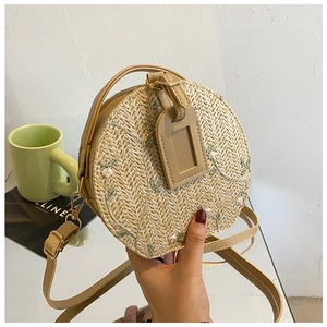 Close-up of bohemian round straw bag featuring floral embroidery and gold hardware
