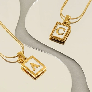 Golden snake chain necklace with embossed alphabet letter A and C pendants on grey surface