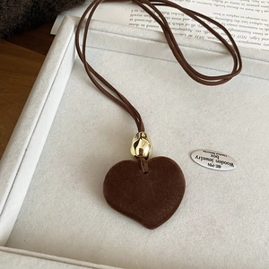 Close-up of brown flocked heart pendant with gold metallic bead on leather cord