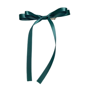 Detailed close-up of dark green satin bow hair clip with elegant long hanging ribbons