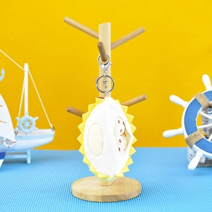 Adorable plush durian fruit keychain charm hanging on a decorative wooden display stand