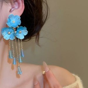 Nahaufnahme von blauen Blumen-Quastenohrringen an einem Model mit eleganten Details