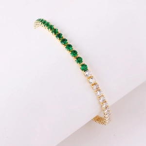 Detail of gold tennis bracelet with alternating emerald green and clear cubic zirconia gems