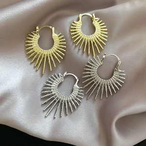 Macro view of gold and silver sunburst hoop earrings on purple silk fabric