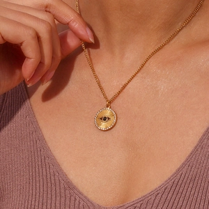 Golden necklace with sunburst coin pendant featuring a black evil eye and white crystals
