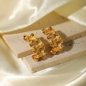 Irregular wavy gold 18K stainless steel earrings on beige stone and silk background