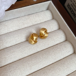 Macro shot of matte gold twisted C-shape earrings on a beige velvet jewelry display pad