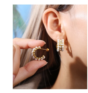 Close-up of gold-plated C-shaped earrings with pearls and crystals on a female model