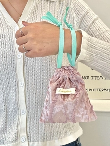 Pink drawstring storage bag with lace trim and Sozakka label held by hand