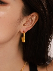 Close-up of a model wearing gold irregular C-shape earrings with a polished mirror finish