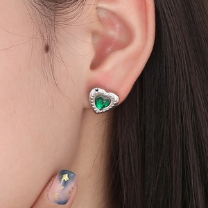 Nahaufnahme eines herzförmigen grünen Kristallohrrings mit Silberfassung am Modellohr