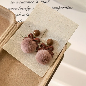 Detailed view of vintage brown ribbon bow earrings with soft fur balls on a poetic card