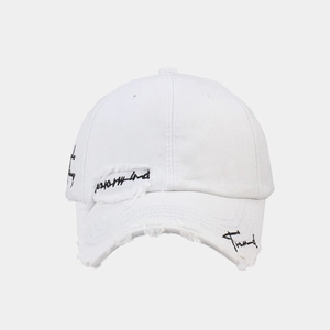 Detailed shot of white vintage cotton baseball cap with distressed rips and black embroidery