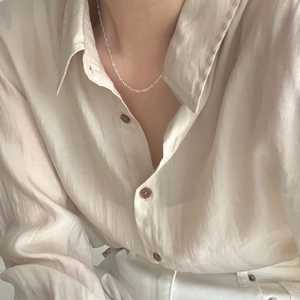 Close-up of minimalist s925 silver phoenix tail chain necklace on beige silk shirt