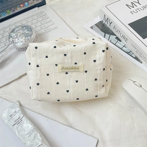 Detail of cream striped makeup bag with black hearts and woven Sozakka label on a desk
