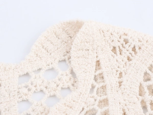 Macro shot of cream white hollow-out crochet knit fabric with intricate floral patterns