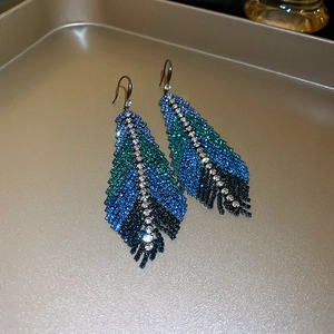 Close-up of sparkling blue and green gradient crystal feather drop earrings on tray