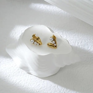 Detail von goldenen Herzohrringen mit weißen Perlen auf einem weißen Deko-Muschelsockel