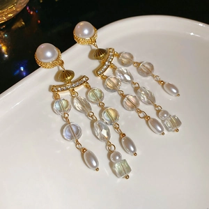 Macro detail of vintage gold pearl earrings with crystal tassels on a ceramic plate