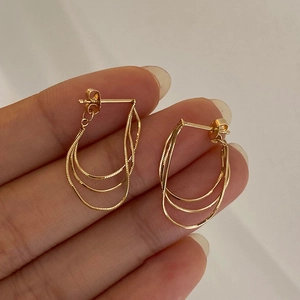 Detail of elegant gold layered chain tassel earrings held to show metallic texture