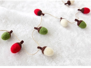 Detail of wool felt acorn garland in red, green and white on plush white background