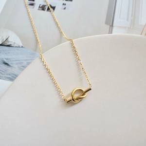 Detailed view of a gold knot pendant necklace on a white elegant jewelry display