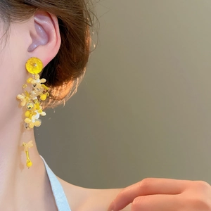 Close-up of elegant yellow fabric flower earrings with pearl tassels on model
