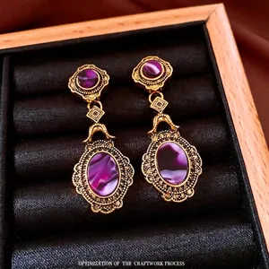 Vintage gold oval drop earrings with purple cat eye stones in a black velvet jewelry box