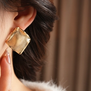 Gros plan de boucles d'oreilles carrées dorées avec texture maillée portées par un modèle