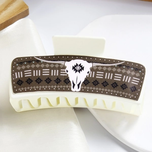 Macro detail of cream hair claw clip with tribal bull head pattern on wooden background