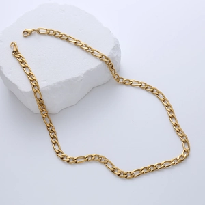 Detail shot of golden Figaro chain necklace draped over a white stone on a white background