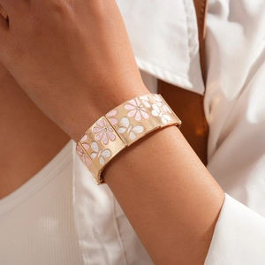 Gros plan d'un large jonc doré avec fleurs en émail rose et blanc sur le poignet d'un mannequin