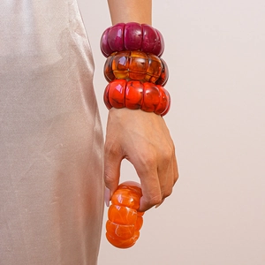 Macro detail of acrylic geometric bangles in amber and burgundy on wrist