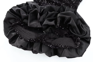Détails d'une robe noire montrant des plis en satin lisse et un patchwork de paillettes