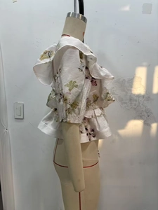 Detail view of white floral ruffle sleeve top with purple flower pattern and linen texture