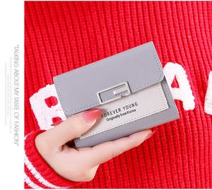 Close-up of a women's short tri-fold color-block wallet held in hand against red background