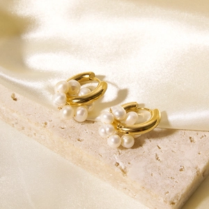 Close-up of gold-plated hoop earrings with natural pearls on beige stone and silk cloth