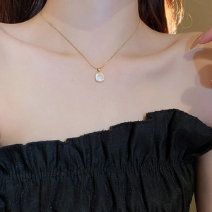 Gros plan détaillé d'un collier pendentif carré en nacre dorée porté autour du cou