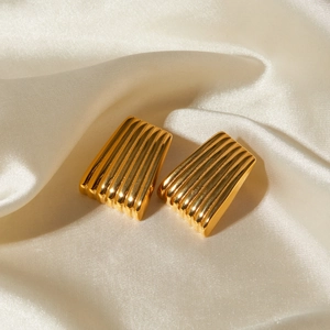 Macro detail of gold striped trapezoid earrings on soft white silk background