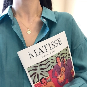 Detail of a gold coin pendant necklace on a model wearing a light blue shirt