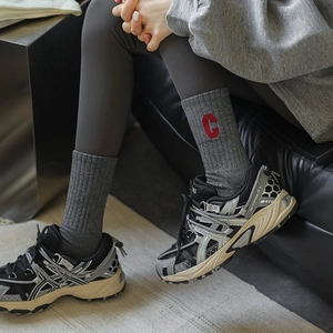 Chaussettes tendance lettre C rouge avec baskets de trail grises sur tapis clair