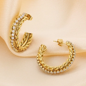 Detail von goldenen C-förmigen Ohrringen mit Kordelstruktur und weißen Zirkonia