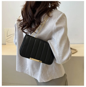 Detail of black vertical striped crossbody bag with gold chain and hardware on model