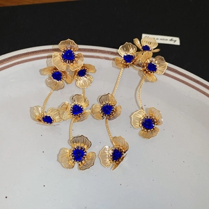 Macro shot of gold floral drop earrings with blue stones on a ceramic plate
