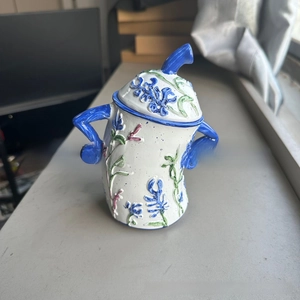 Detail of creative ceramic jar featuring blue 3D floral relief and unique sassy arm handles