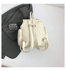 Rear view of off-white faux leather backpack with adjustable straps on grey blazer background