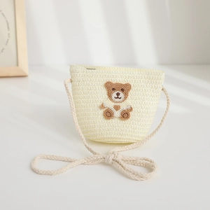 Detail view of a cream straw crossbody bag for kids with a cute bear patch and rope strap